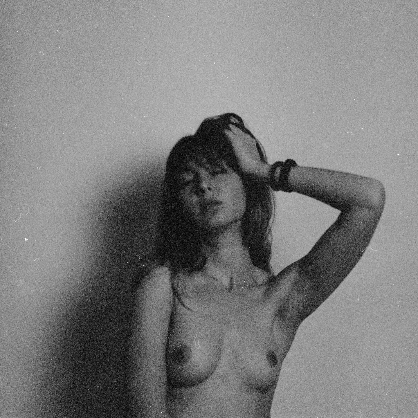 A topless woman with her eyes closed and one arm raised is captured in a black and white portrait.
