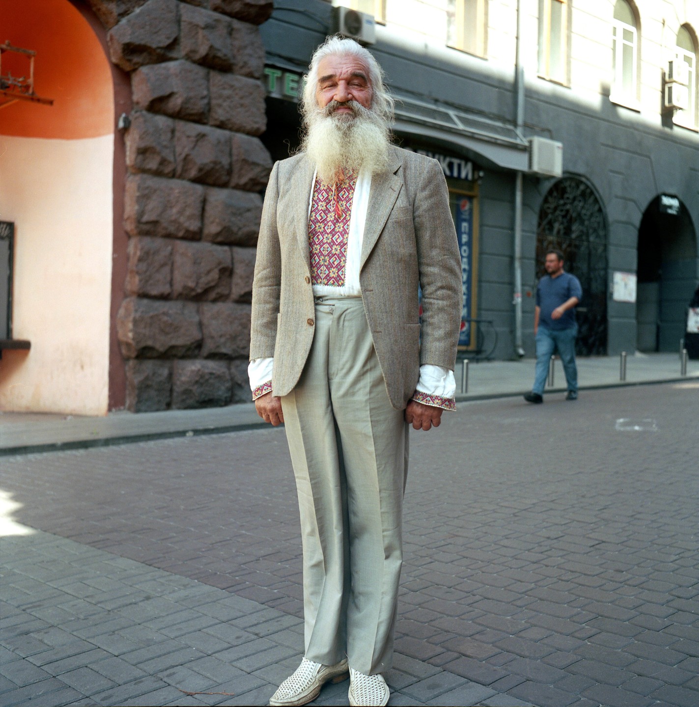 A man with a long white beard and embroidered shirt stands on a cobblestone street in Kyiv.
