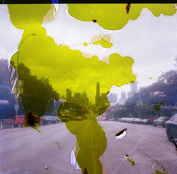 A street leads to a city skyline, partially obscured by yellow and white patterns.