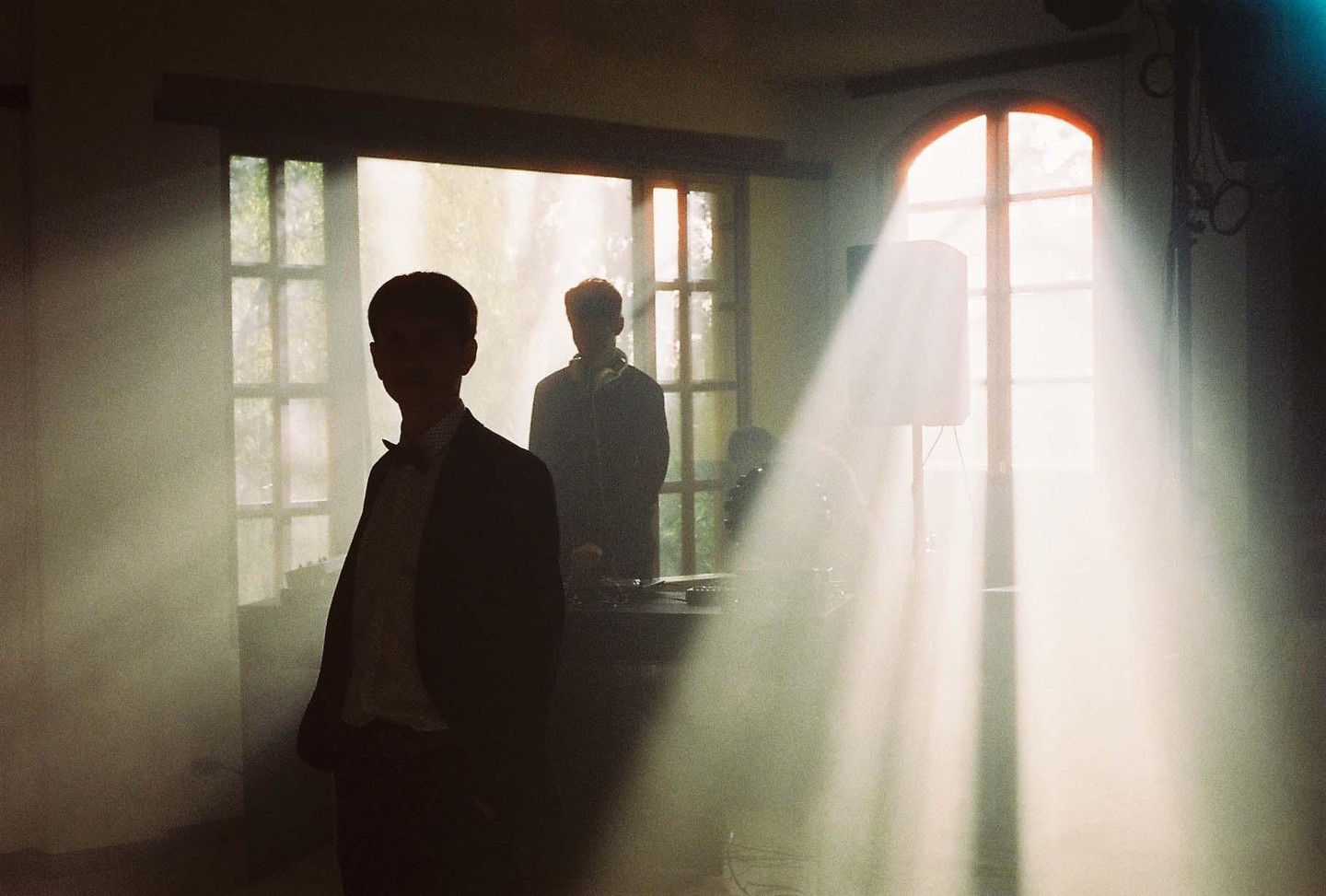 Two men are silhouetted by bright light streaming through windows in a hazy room.