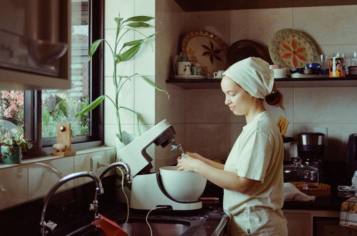 A woman wearing a headscarf is preparing food with a stand mixer in a kitchen.