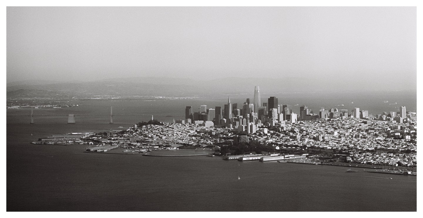 An aerial view shows the San Francisco skyline and bay with bridges in the distance.