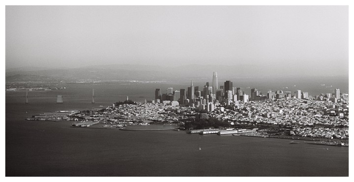 An aerial view shows the San Francisco skyline and bay with bridges in the distance.