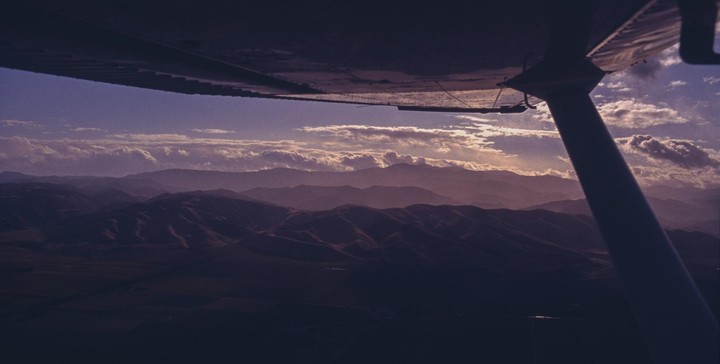 A view from an airplane shows mountains and clouds at sunset.
