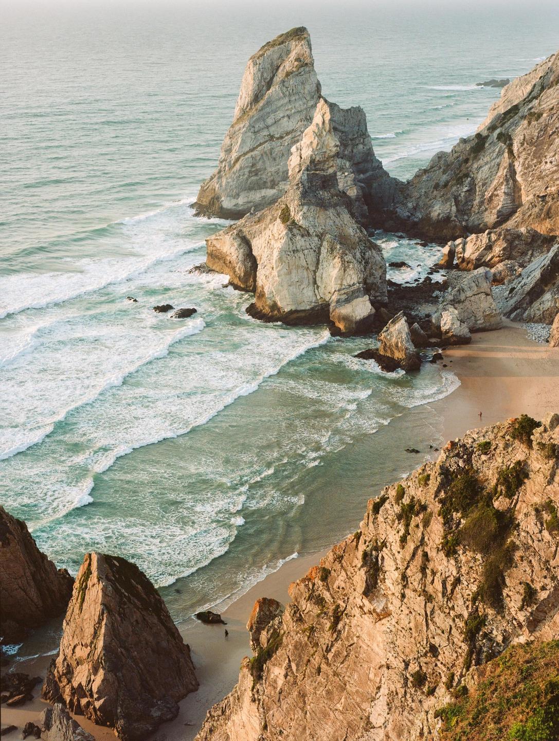 Waves crash on a sandy beach surrounded by large rock formations.