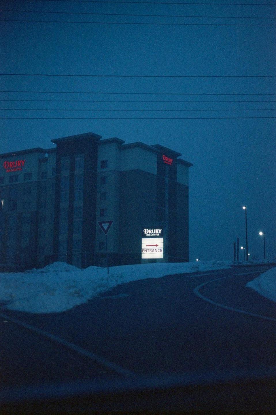 A hotel building with illuminated signs stands beside a snow-covered road at night.