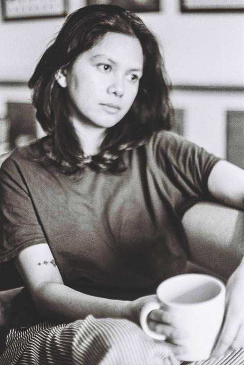 A woman with long hair sits holding a mug, looking away from the camera.