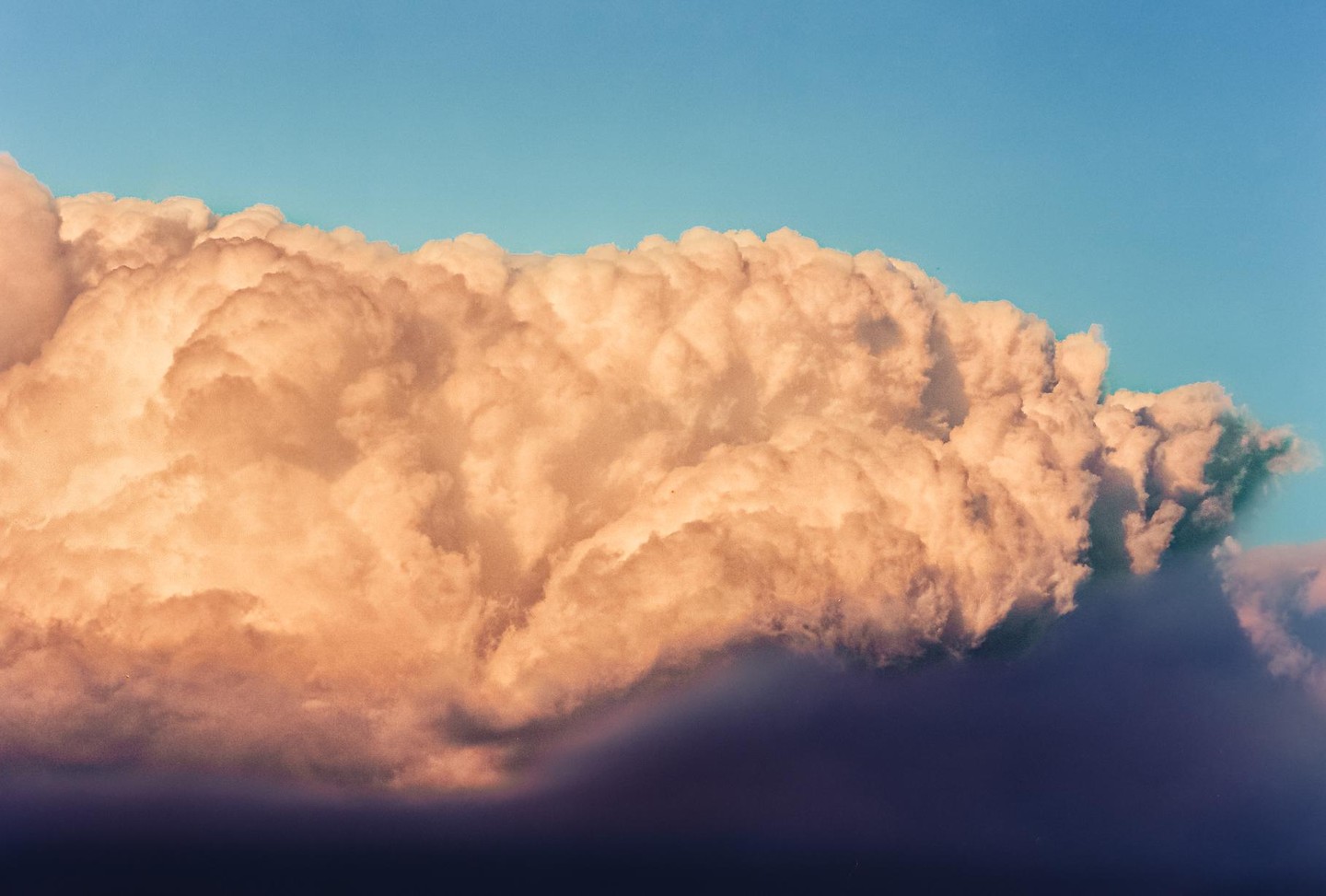 A large, fluffy cloud formation fills the sky, with its upper portion illuminated by warm light and its lower portion in shadow.