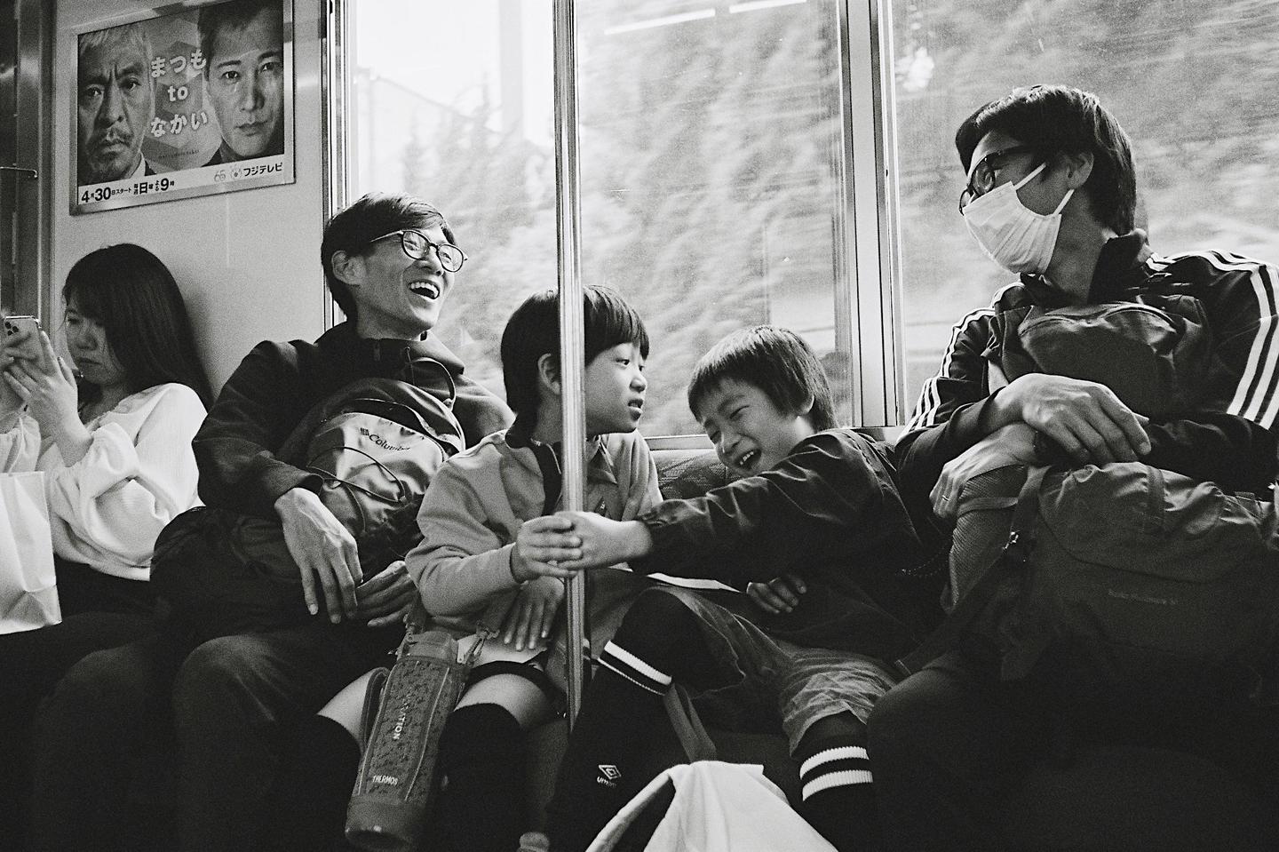 People are sitting on a train, with one man laughing and two children interacting.