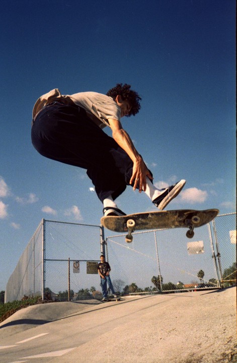 A man performs a skateboard trick in a skate park under a clear blue sky.