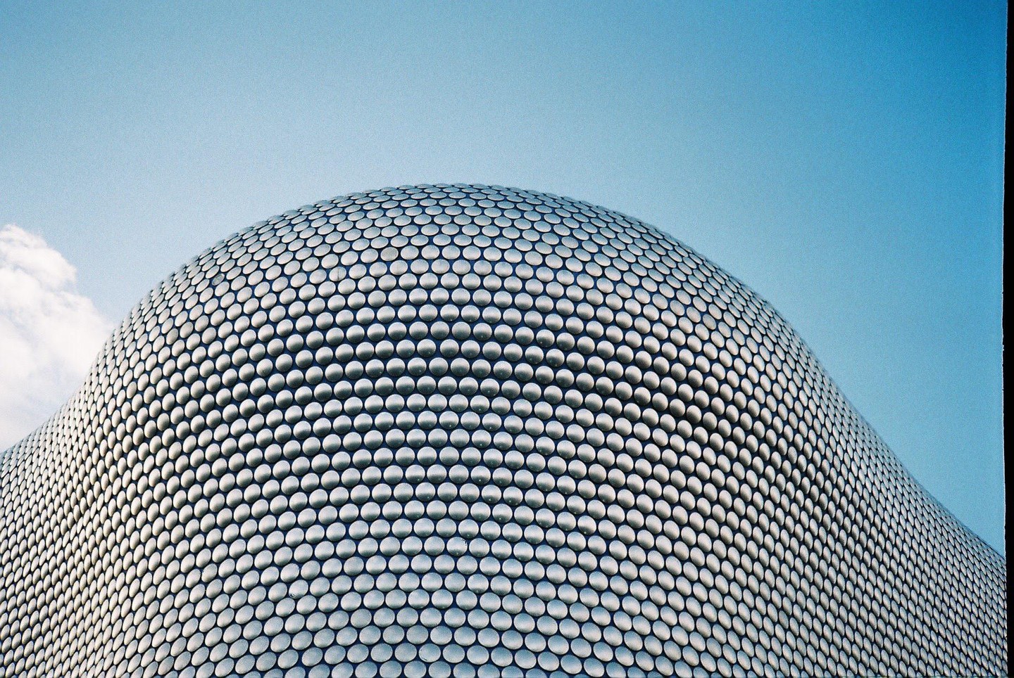 A modern building with a textured facade made of many small circles curves against a clear blue sky.