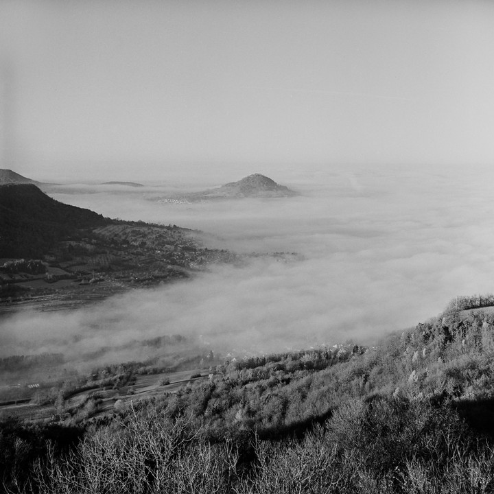 A landscape view shows a valley filled with fog, with hills and a town visible above the fog.