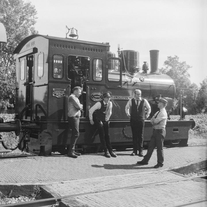 Four men stand on a brick platform next to a train.