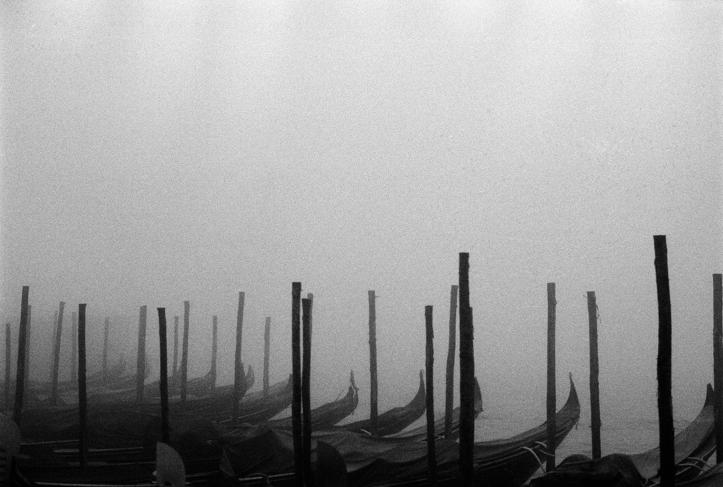 Gondolas are moored in a foggy canal in Venice.