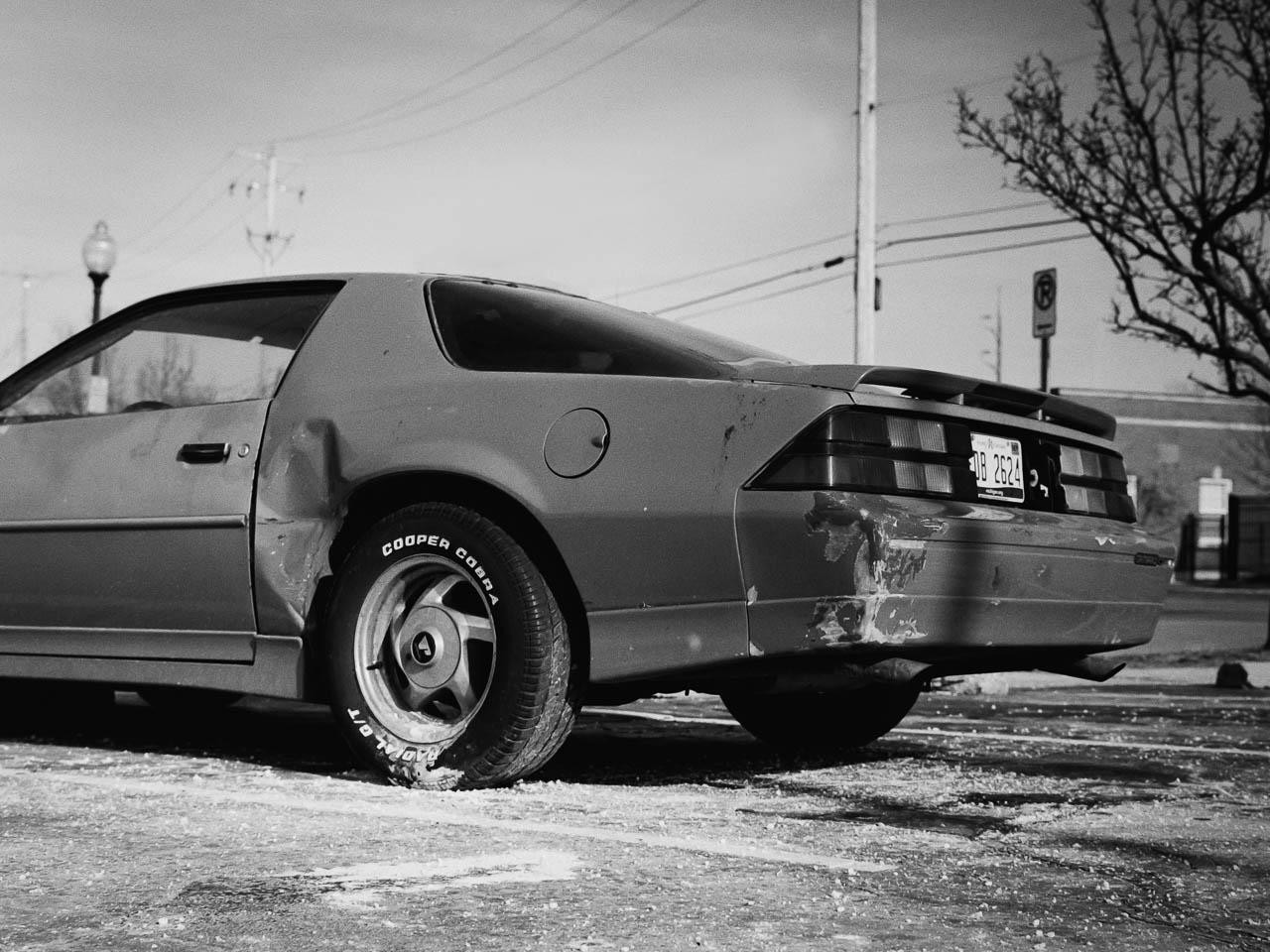 A damaged car with a flat tire is parked on a street.