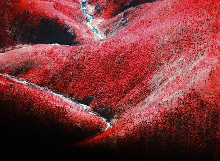 An aerial view shows a winding river through red-hued mountains.