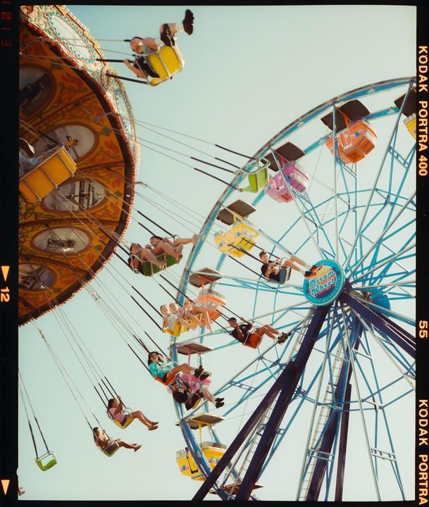 People are riding a swing ride and a ferris wheel at an amusement park.