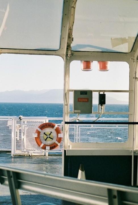 A life preserver hangs on the railing of a boat with the ocean and mountains in the background.