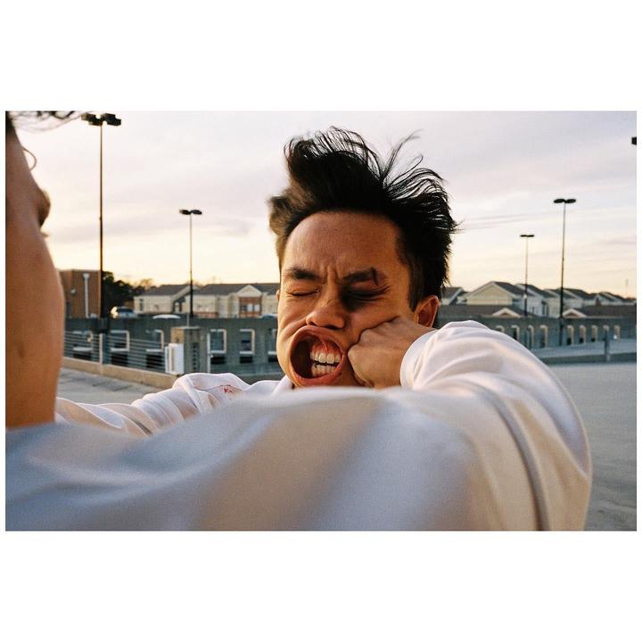 A man is punched in the face by another person, distorting his features and making his hair fly up.