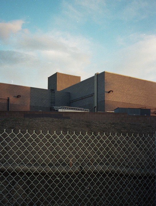 A chain link fence stands in front of a building with a blue sky overhead.