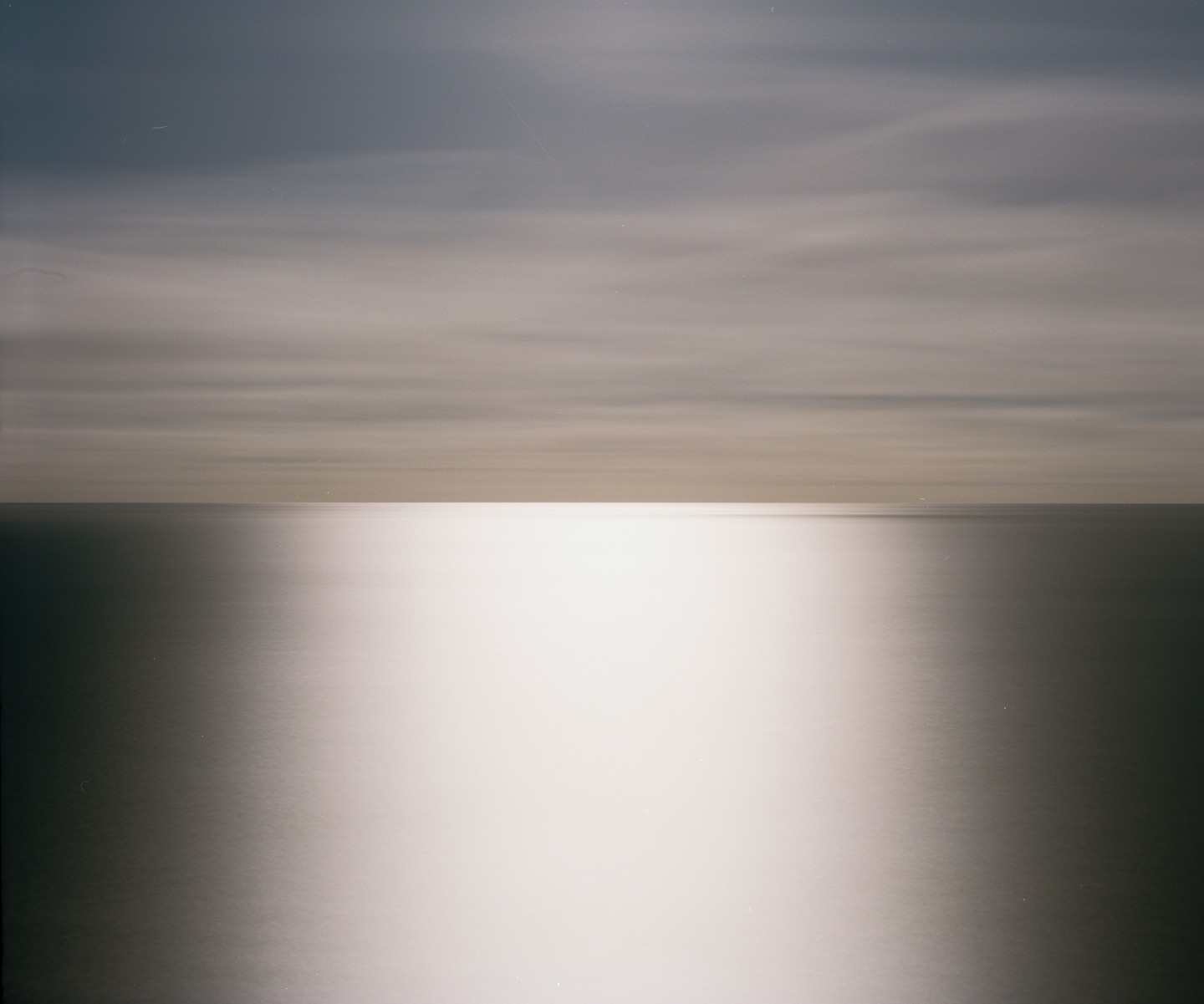 The ocean meets the sky under a bright light reflecting on the water.