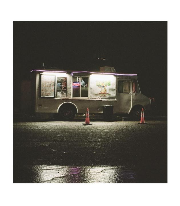 A food truck with glowing lights is parked on a wet street at night.