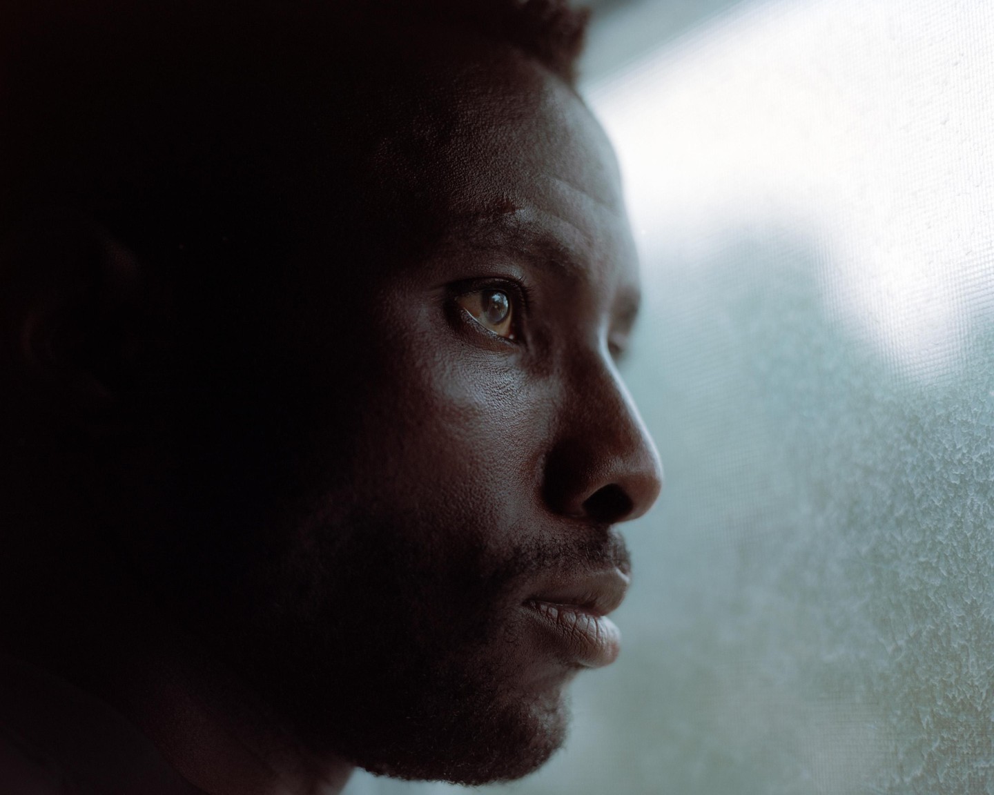 A man looks out a window with light reflecting in his eye.