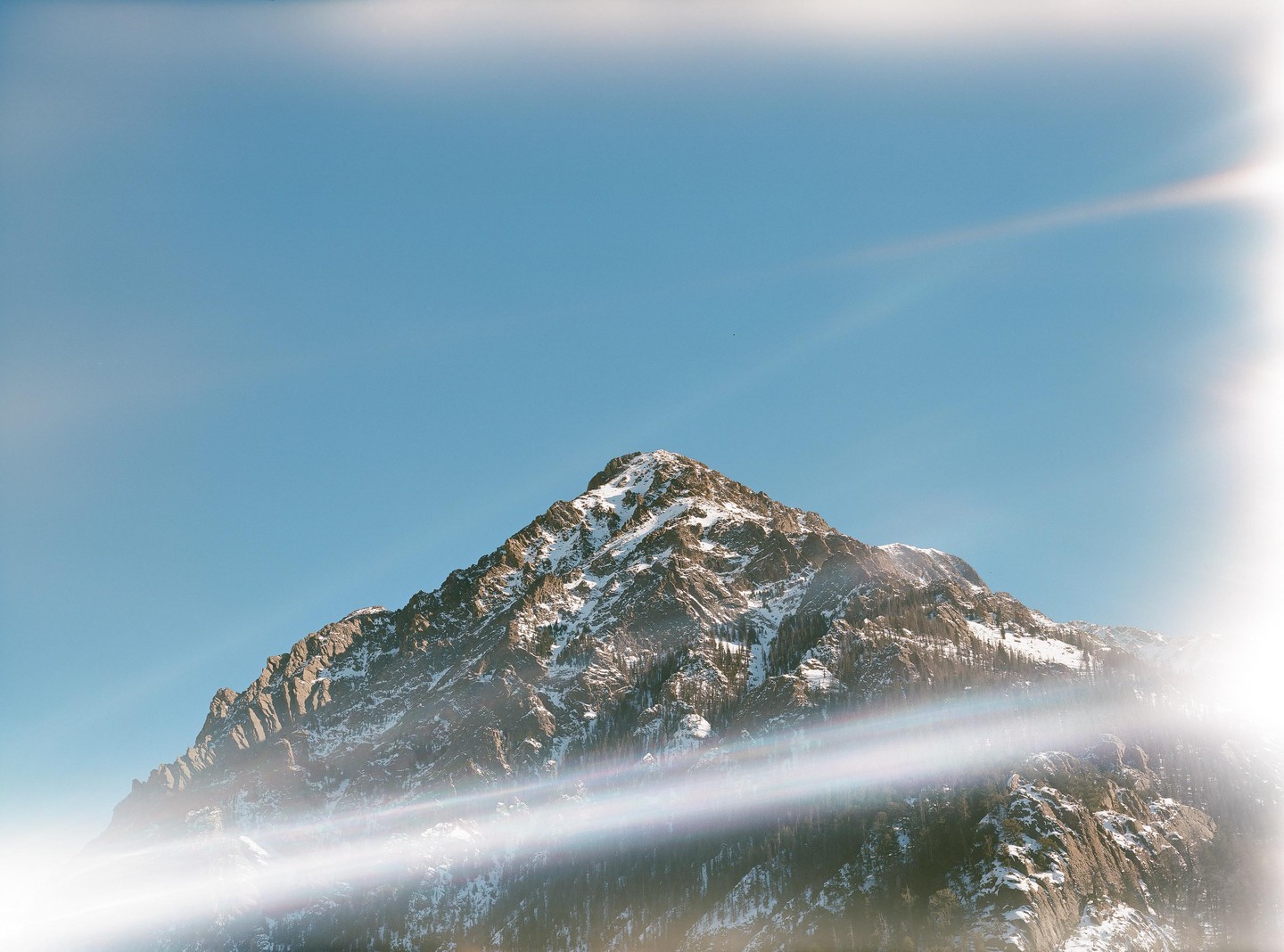 A snow-capped mountain peak rises against a clear blue sky with prominent light leaks.