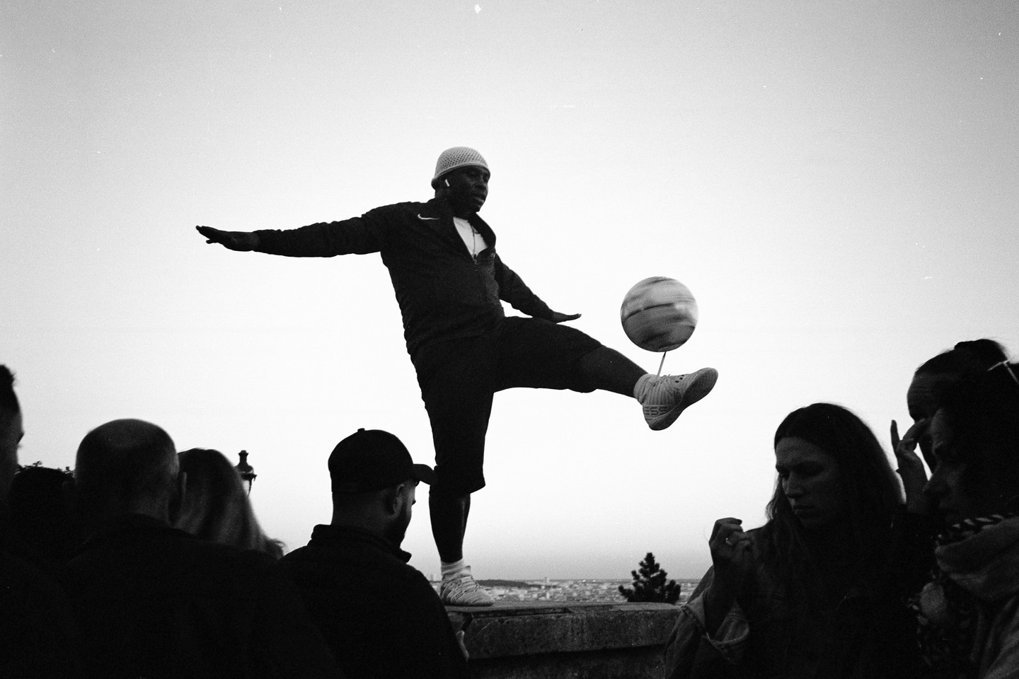 A man balances a spinning soccer ball on his foot while performing for a small crowd.
