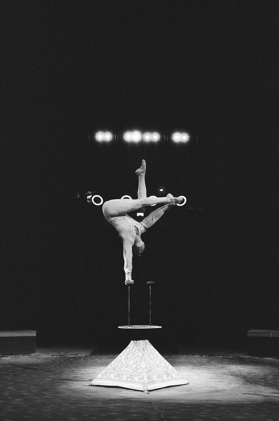 A woman performs a handstand on a small platform with her legs extended in a split.