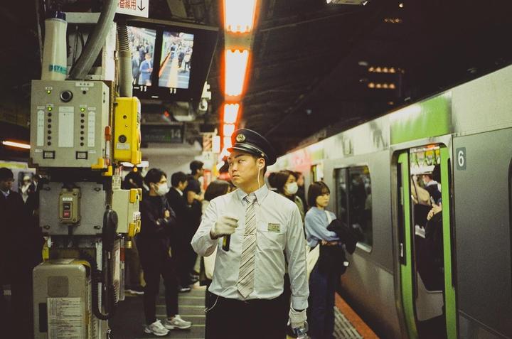 A man in a uniform stands on a subway platform next to a train with its doors open.