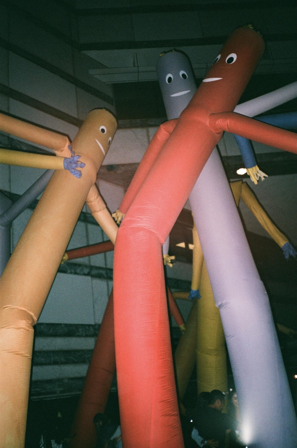 Several colorful inflatable tube men with faces and arms stand together in a dark room.