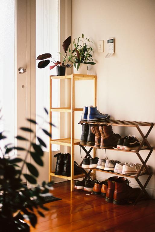 A wooden shoe rack with many pairs of shoes sits next to a door and a plant stand with potted plants.
