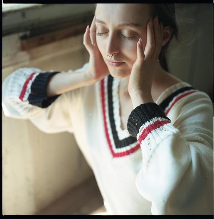 A woman with closed eyes and a nose piercing holds her head in her hands.
