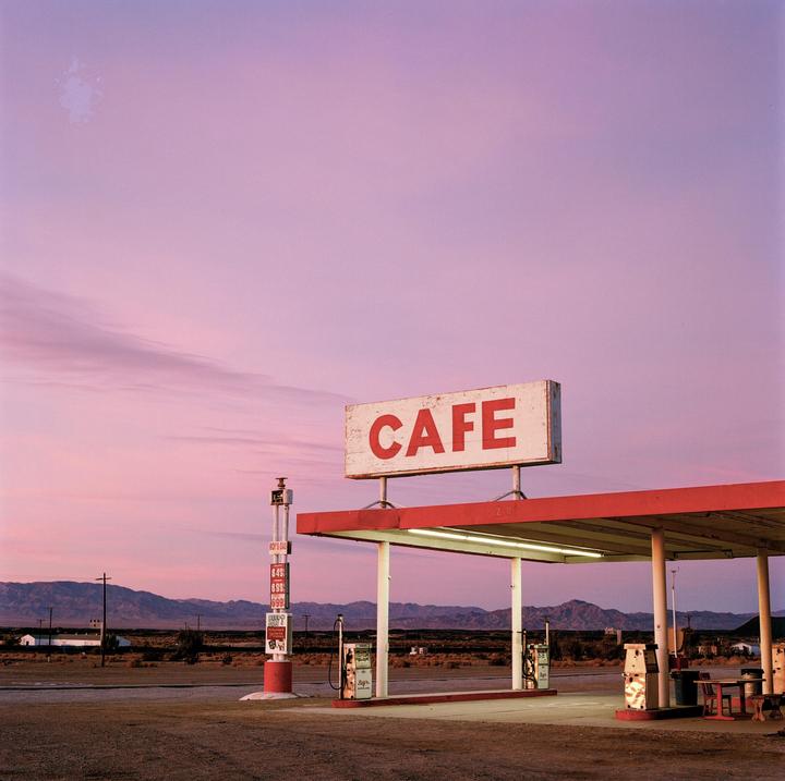 A gas station with a "CAFE" sign is visible under a pink and purple sky at dusk.