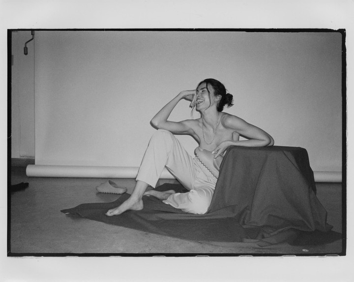 A woman sits on the floor next to a draped table, laughing with her hand to her face.