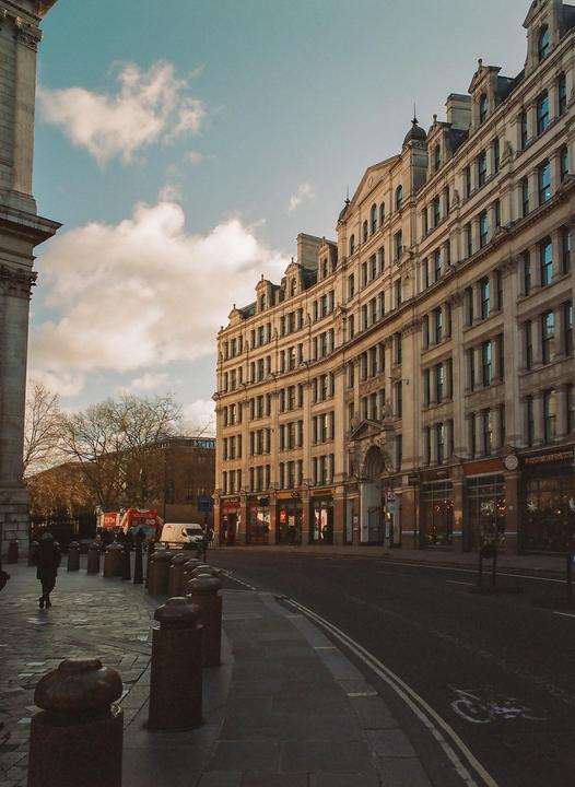 A street in London is lined with tall, ornate buildings under a partly cloudy sky.
