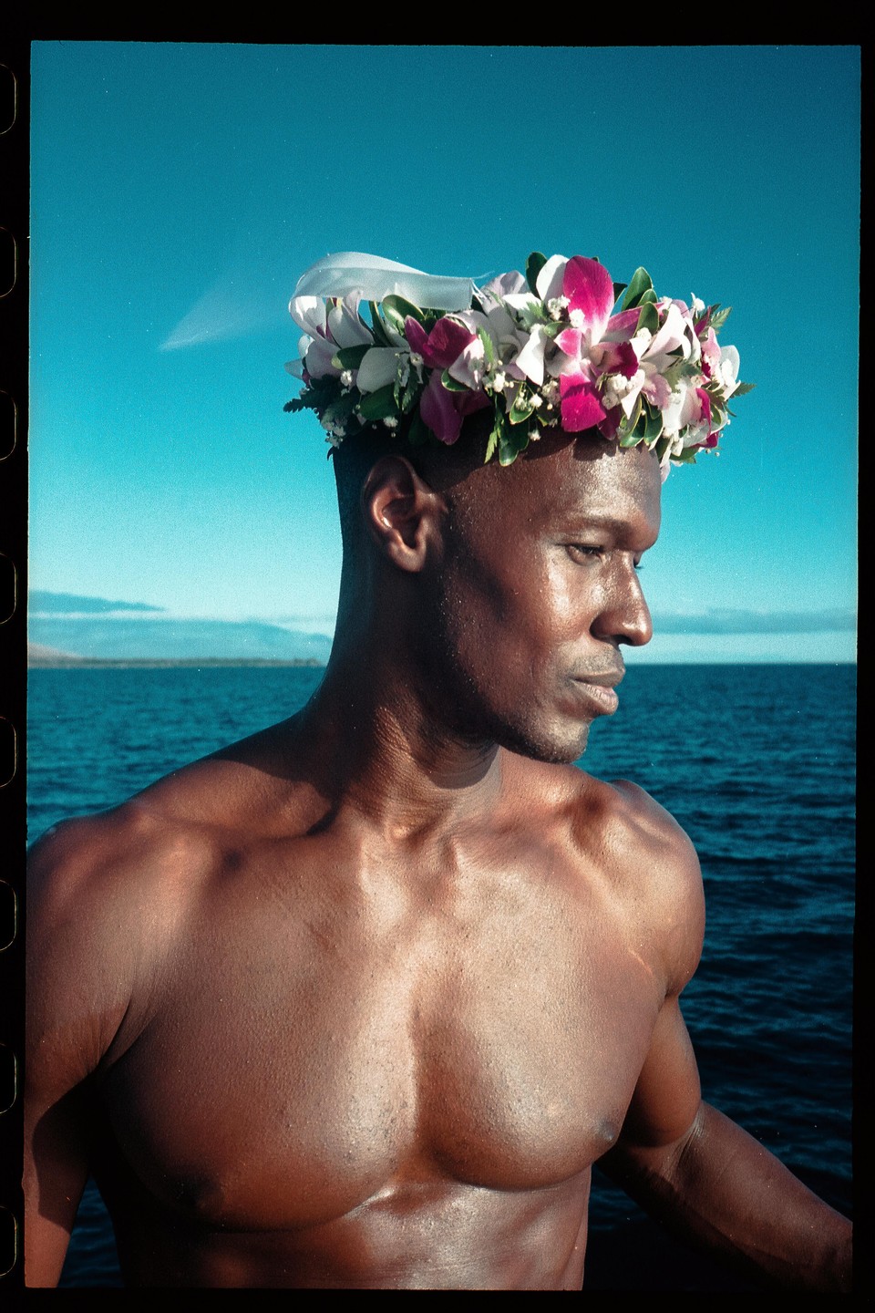 A man wearing a flower crown looks out over the ocean.