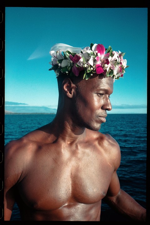 A man wearing a flower crown looks out over the ocean.