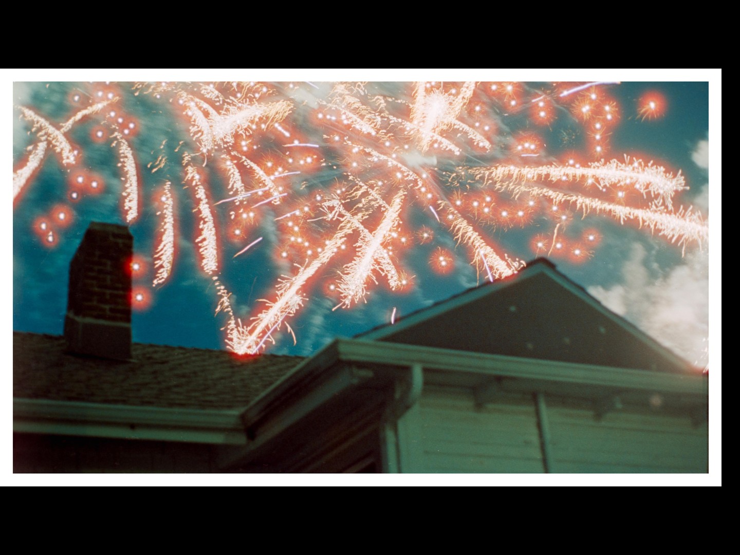 Fireworks explode in the night sky above a house.