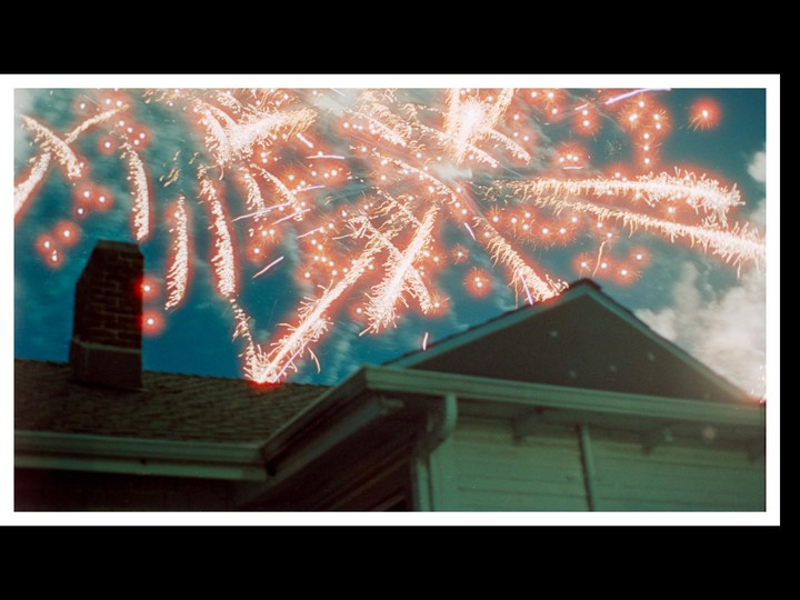 Fireworks explode in the night sky above a house.