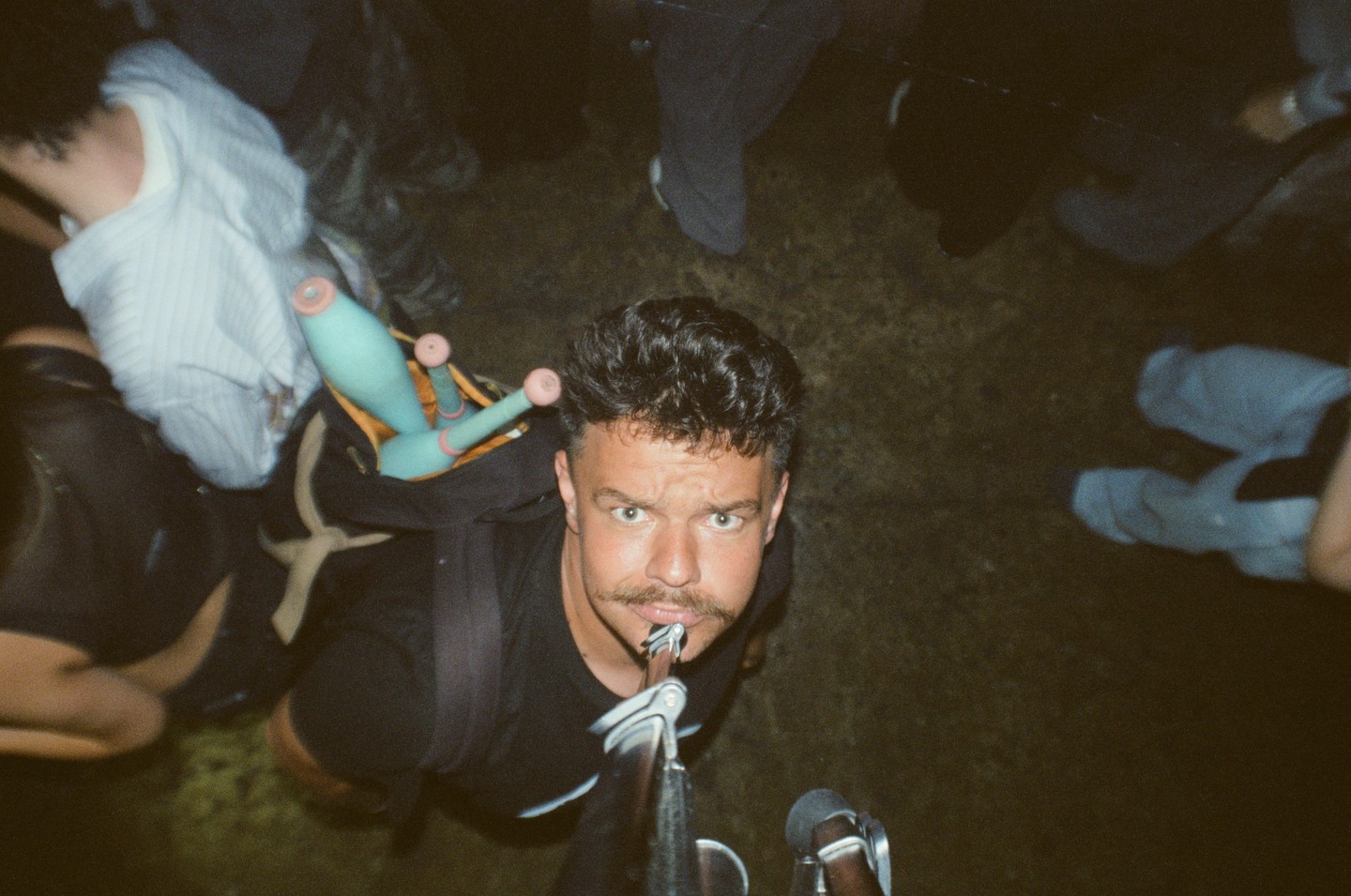 A man with a mustache balances a tripod on his chin while looking up at the camera.