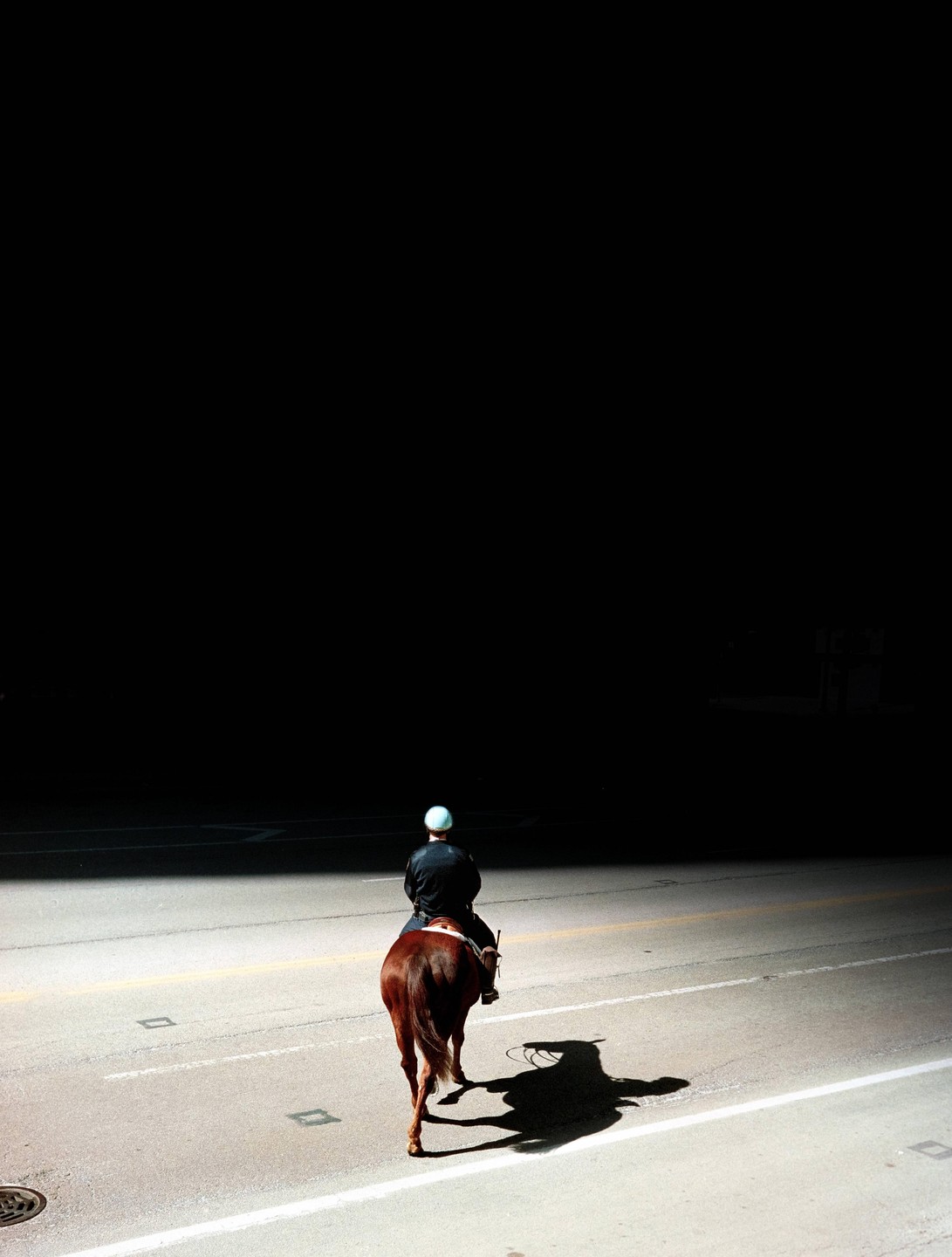 A person on horseback rides down a street with a long shadow cast behind the horse.