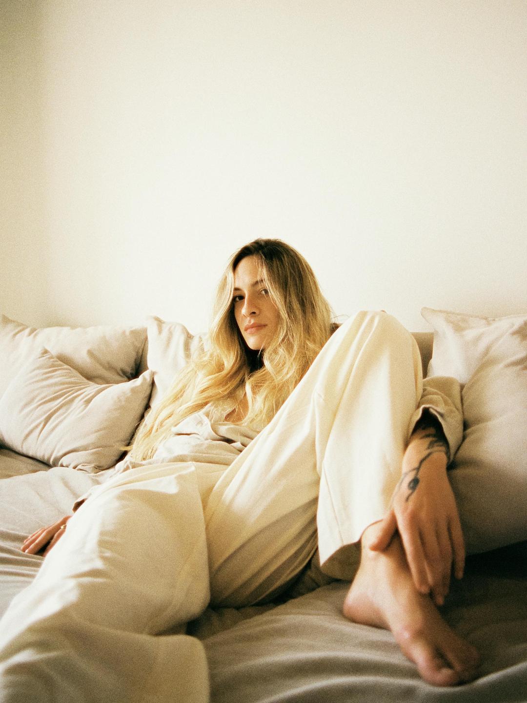 A woman with long hair is sitting on a bed with pillows.