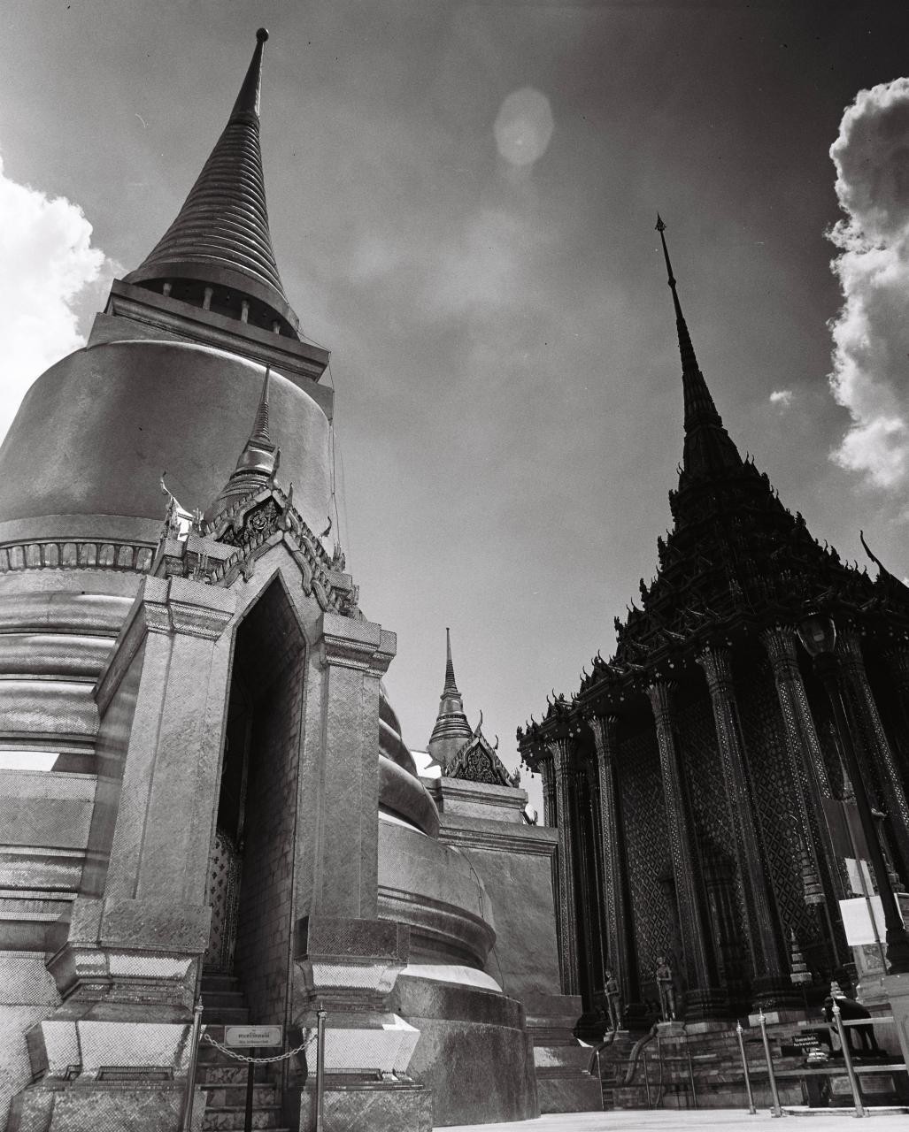 Two ornate temple spires rise towards a cloudy sky, with a large stupa on the left and a dark, intricate building on the right.