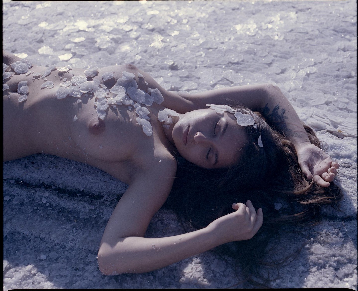 A woman lies on a bed of salt crystals with more crystals scattered across her body.