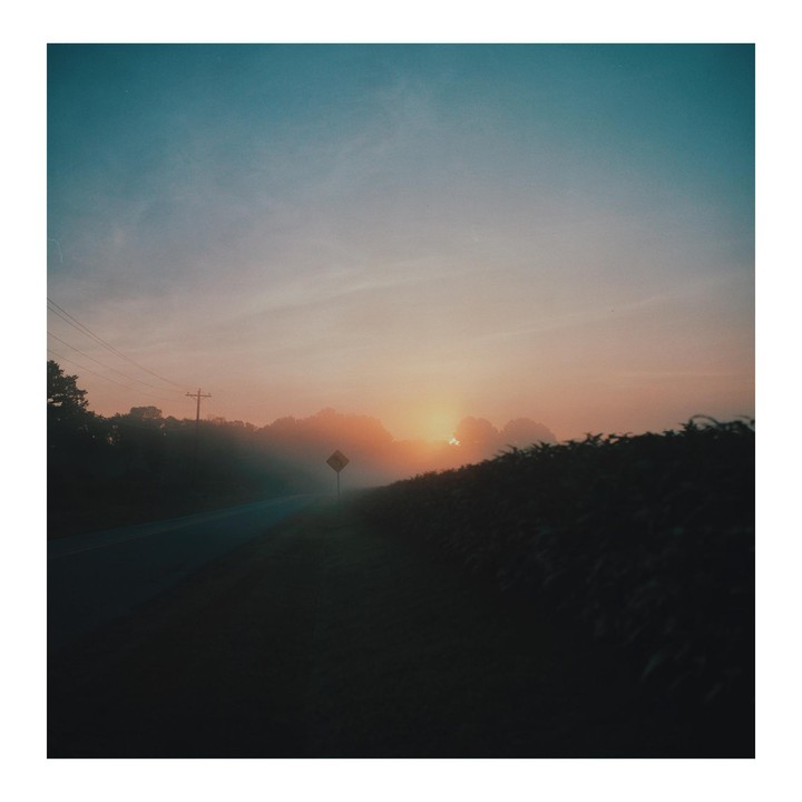 A road sign is visible through the fog on a road at sunset.