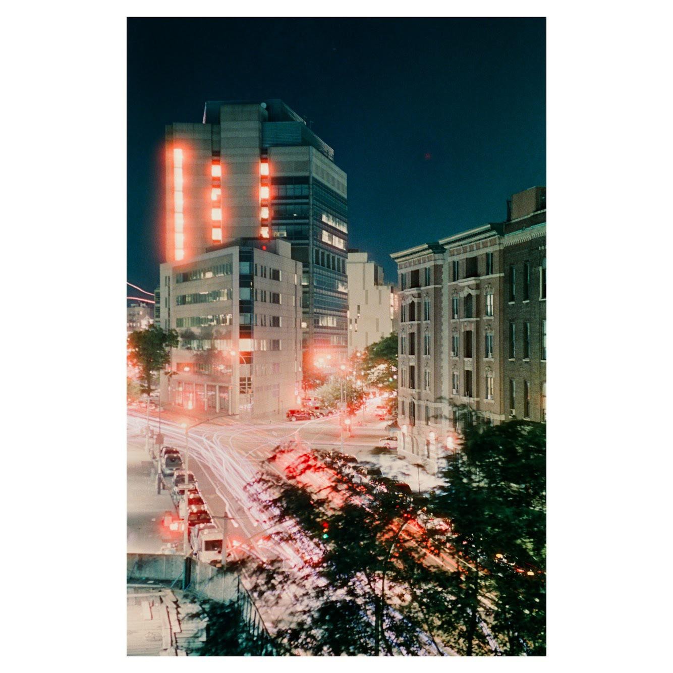 A city street is visible at night with light trails from vehicles and illuminated buildings.