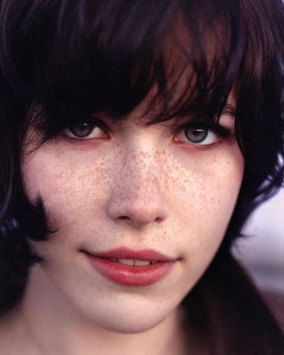 A woman with dark hair and freckles looks directly at the viewer.