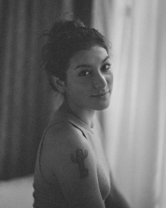A woman with a cactus tattoo on her shoulder looks over her shoulder at the viewer.